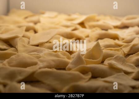 Knödel, Knödel, Ravioli. Sperrholzschneidebrett, Holzmehlsieb und Walzstift - Werkzeuge zur Herstellung von Teig. Stockfoto