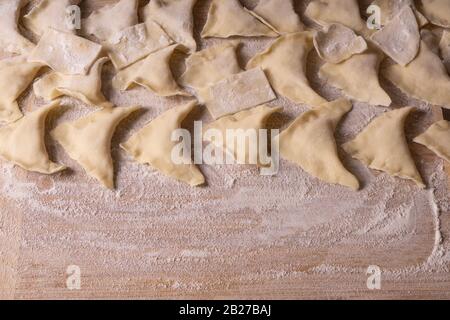 Knödel, Knödel, Ravioli. Sperrholzschneidebrett, Holzmehlsieb und Walzstift - Werkzeuge zur Herstellung von Teig. Stockfoto