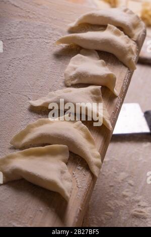 Knödel, Knödel, Ravioli. Sperrholzschneidebrett, Holzmehlsieb und Walzstift - Werkzeuge zur Herstellung von Teig. Stockfoto