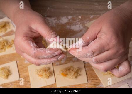 Eine Frau sculpt Knödel und Ravioli aus Kneten und Kohl. Sperrholzschneidplatte, Holzmehlsieb und Walzstift aus Holz - Werkzeuge für Stockfoto