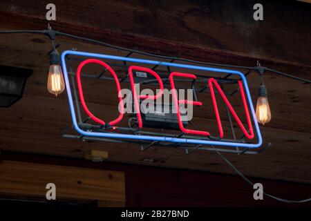 Rotes und blaues offenes Schild mit Neonlicht, das an einem bewaldeten Rand hängt Stockfoto