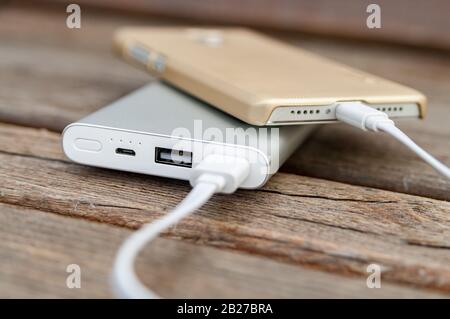 Smartphone wird mit powerbank auf der Bank aufgeladen. Stockfoto