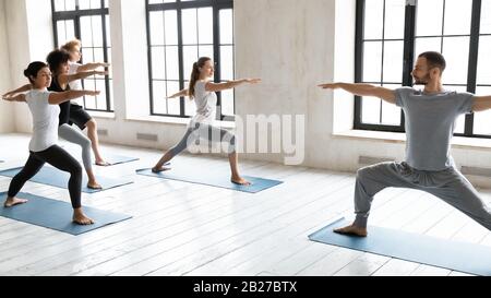 Trainer und Vielvölkerige stehen in Warrior Two Yoga-Position Stockfoto