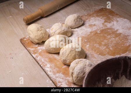 Teigkugeln. Sperrholzschneidebrett, Holzmehlsieb und Walzstift - Werkzeuge zur Herstellung von Teig. Stockfoto