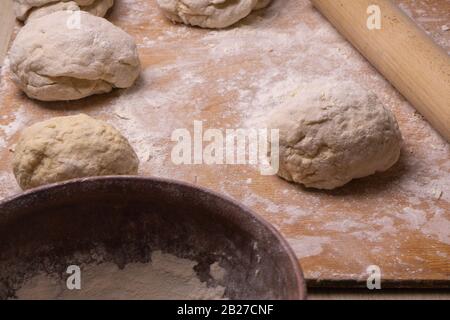 Teigkugeln. Sperrholzschneidebrett, Holzmehlsieb und Walzstift - Werkzeuge zur Herstellung von Teig. Stockfoto