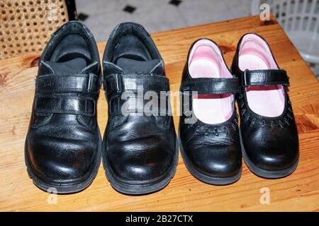 Zwei Paar schwarze Schulschuhe aus Leder, ein Jungen, ein Mädchen, poliert und bereit zum tragen auf einem Holzkitchentisch Stockfoto