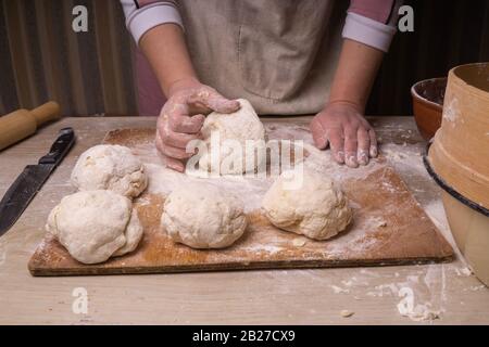 Eine Frau knetet den Teig. Sperrholzschneidebrett, Holzmehlsieb und Walzstift - Werkzeuge zur Herstellung von Teig. Stockfoto