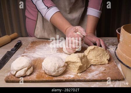 Eine Frau knetet den Teig. Sperrholzschneidebrett, Holzmehlsieb und Walzstift - Werkzeuge zur Herstellung von Teig. Stockfoto