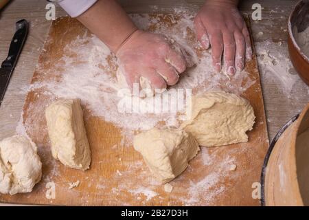 Eine Frau knetet den Teig. Sperrholzschneidebrett, Holzmehlsieb und Walzstift - Werkzeuge zur Herstellung von Teig. Stockfoto