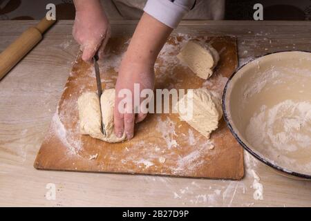 Eine Frau knetet den Teig. Sperrholzschneidebrett, Holzmehlsieb und Walzstift - Werkzeuge zur Herstellung von Teig. Stockfoto