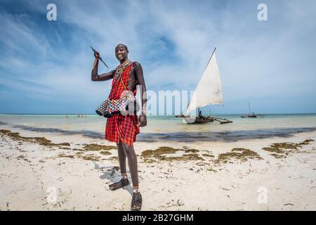 Diani Beach/Kenia - 01. März 2020: Masai am Strand in Kenia, Diani Beach, watamu hält einen Pfeil mit einem Segelboot im Hintergrund Stockfoto