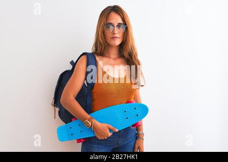 Junge Rothirdschülerin mit Rucksack und Skateboard über isoliertem Hintergrund mit einem selbstbewussten Ausdruck auf einem klugen Gesicht, das ernsthaft denkt Stockfoto