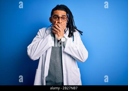 Junger afroamerikanischer Arzt mit Dreadlocks, die Stethoskop und Brille tragen, schockiert den Mund mit den Händen aus versehen. Geheimes Konzept. Stockfoto