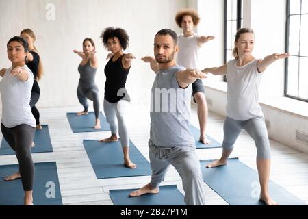 Sieben multiethnische Menschen, die Yoga üben, indem sie Krieger II posieren Stockfoto
