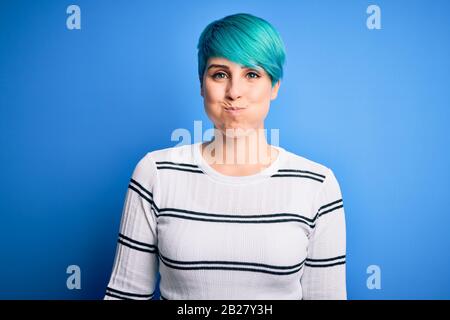 Junge schöne Frau mit blauem Modehaar mit legeren Pullover, die an den Wangen des Studios mit lustigem Gesicht steht. Mund aufgeblasen mit Luft, verrückt Stockfoto