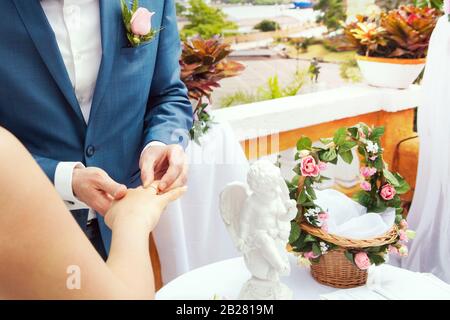 Die Hand des Bräutigams, die einen Hochzeitsring auf den Finger der Frau legt Stockfoto