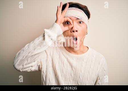 Der junge, gutaussehende chinese wurde wegen eines Unfalls verletzt, der Bandage und Streifen auf dem Kopf trug, was eine Geste war, die mit einem überraschten Gesicht schockiert war, das Auge sah durch f Stockfoto