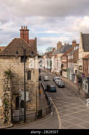 Blick über die Straßenkreuzung von Bootham in York. Die Fahrzeuge warten an der Ampel neben einem alten Torategebäude mit einer zerfallenden Mauer. Stockfoto