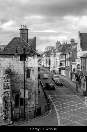 Blick über die Straßenkreuzung von Bootham in York. Die Fahrzeuge warten an der Ampel neben einem alten Torategebäude mit einer zerfallenden Mauer. Stockfoto