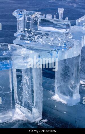 Auf dem Eis des Baikalsee steht die Figur einer alten Dampflok aus Eis. Der Zug besteht aus klarem blauem Eis. Vertikal. Stockfoto