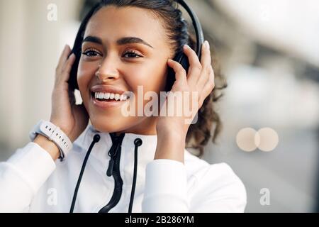 Fröhliche junge Frau mit Kopfhörern, die nach dem Training Musik in der Stadt hören Stockfoto