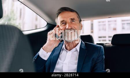 Lächelnder älterer Mann, der auf dem Handy spricht, während er im Taxi sitzt und wegschaut Stockfoto