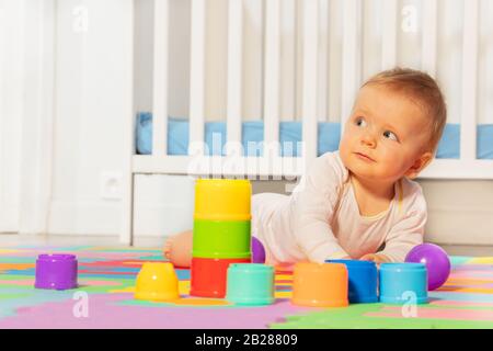 Schöner Kleinkind Junge, vor Krippe mit Spielzeug auf dem Teppich krabbeln Stockfoto