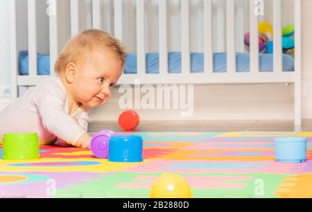 Kleine Kleinkinder schleichen sich auf dem Boden des Kindergartens mit bunten Spielzeugen Stockfoto