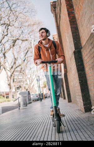 Porträt des jungen lateinmannes, der auf der Straße der Stadt einen Elektroscooter fährt. Modernes und ökologisches Transportkonzept. Stockfoto