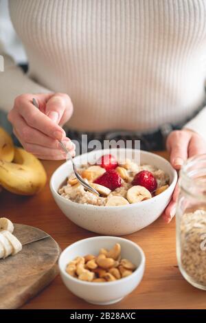 Haferbrei Haferbrei mit Bananen und Erdbeeren, gesundes Frühstück. Frau, die vegane oder vegetarische, gesunde Frühstückschüssel isst Stockfoto