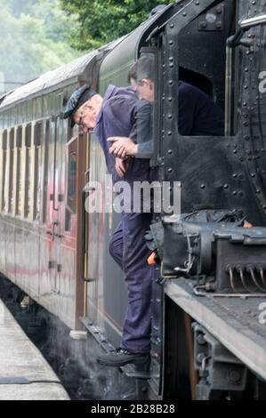 Ein Lokführer alcht die Fußplatte eines Personendampfzugs der North Yorkshire Moors Railway am Bahnhof Goathland am North York Mo Stockfoto