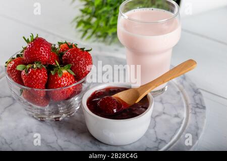 Erdbeermarmelade und Erdbeerpinkmilch aus Glas auf dem marmornen Servicestboden Stockfoto