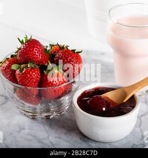 Erdbeermarmelade und Erdbeerpinkmilch aus Glas auf dem marmornen Servicestboden Stockfoto