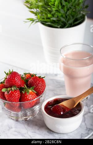 Erdbeermarmelade und Erdbeerpinkmilch aus Glas auf dem marmornen Servicestboden Stockfoto