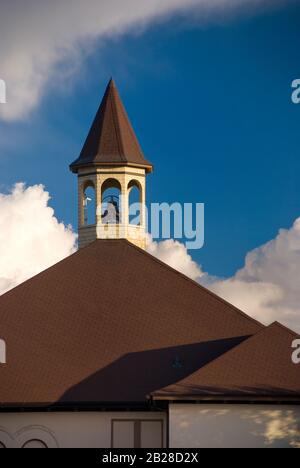 Tall Brown öffnete den Kirchturm mit einer großen Metallglocke über einem braunen Dach-Kirchengebäude unter dem blauen und trüben Himmel Stockfoto