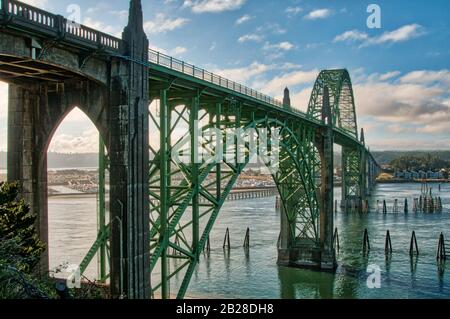 Lange Beton- und Grünhälfte durch grün geruttete Bogenbrücke, die von einem Ansatz auf die andere Seite des Flusses blickt Stockfoto