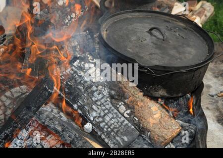 Die große Black 16-Zoll-Lodge Camp Dutch Oven befindet sich im heißen Feuer und kocht eine Mahlzeit Stockfoto