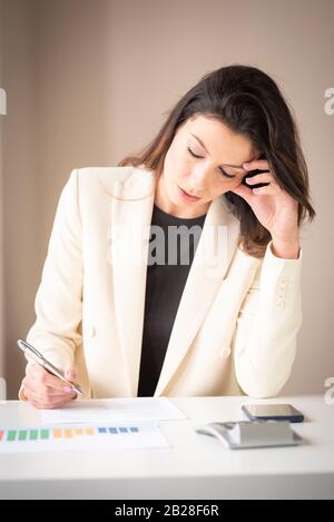 Schuss von einer Geschäftsfrau, die am Schreibtisch sitzt und nachdenklich aussieht, während sie etwas Papier macht. Stockfoto