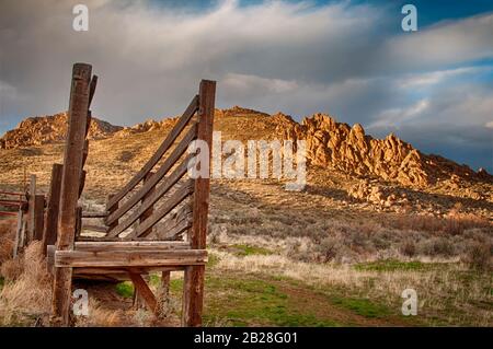 Die Laderampe aus Holzrindern liegt auf der schattigen Seite der Hügel, wobei das Sonnenlicht die höher gelegenen Felshänge des Owyhee County Idaho beleuchtet Stockfoto