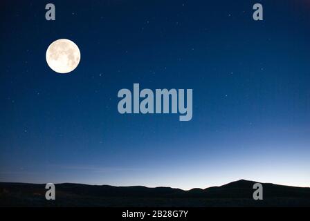 Großer Vollmond während der brechenden Dämmerung Licht über den Horizont am frühen Morgen mit den Sternen, die noch am Himmel zu sehen sind Stockfoto