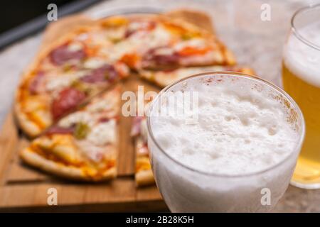 Frisches Bier im Glas mit Hausgemachter Pizza im Hintergrund. Selektiver Fokus Stockfoto