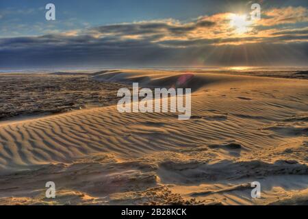 Orangefarbene Sonne Hinter den Wolken, die den Horizont des Pazifischen Ozeans vor der Küste von Oregon umrahmen und die Strandsand-Salzung und das salzende gr beleuchten Stockfoto