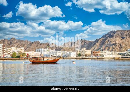 Altes Segelboot in Muttrah Corniche verankert. Die Altstadt und die Berge im Hintergrund. Aus Maskat, Oman. Stockfoto