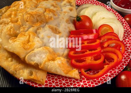 Pikante Pastete mit Wurstfleisch mit Tomaten, süßem Pfeffer und Ketchup liegt in einer flachen Platte auf einem dunklen Holztisch. Köstliche hausgemachte Speisen. Nahaufnahme. Stockfoto