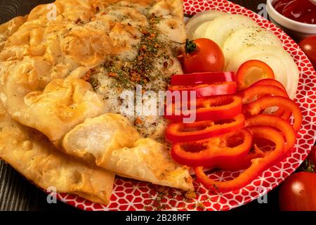 Würziger PIE-Spüro mit Fleisch, mit Gewürzen bestreut, mit Tomaten, süßem Pfeffer und Ketchup liegt in einer flachen Platte auf einem dunklen Holztisch. Köstliches ho Stockfoto