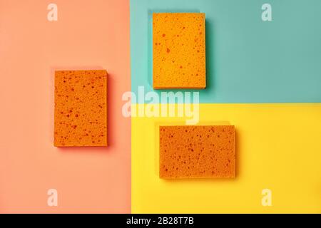Trendige Collage aus orangefarbenen Schwämmen auf gelbem, rosafarbenem Korallen und trendigen mintgrün-blauen Hintergrund. Flache Lage, Draufsicht, Nahaufnahme. Minimaler Stil. Stockfoto
