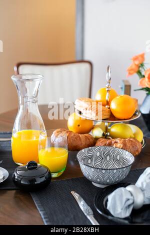 Ein köstliches kontinentales Frühstück mit frisch gebackenem Blätterteig und gepresstem Orangensaft, das auf einem dunklen Holztisch serviert wird. Stockfoto