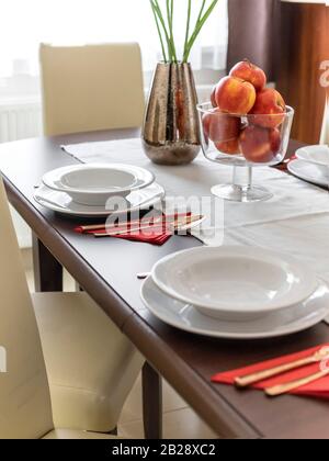 Geschirr und eine große Schüssel Obst auf einem Esstisch in natürlichem Licht, angewinkelt. Stockfoto