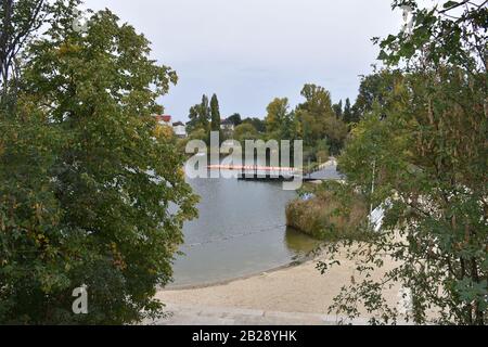 Ein See mit einem sandigen Strand und einem Minikastdock. Viel Grün. Die Blätter der Bäume fingen an, gelb zu werden. Stockfoto