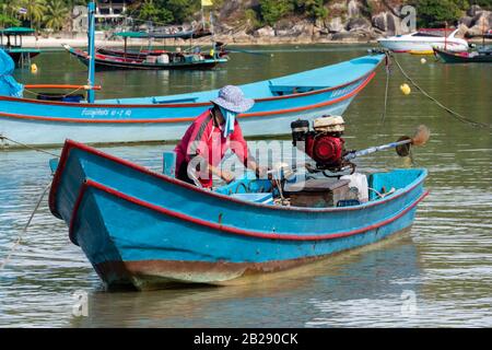 Eine thailänderin, die an einem Strand in Thailand ein Fischglongtail-Boot im flachen Wasser vorbereitet. Stockfoto